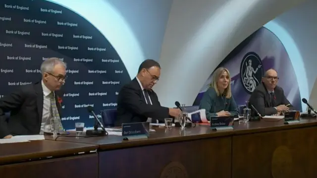 Bank Of England Press Conference Hack Bank of England Governor Mark Carney at a press conference podium with microphones and audio equipment visible.