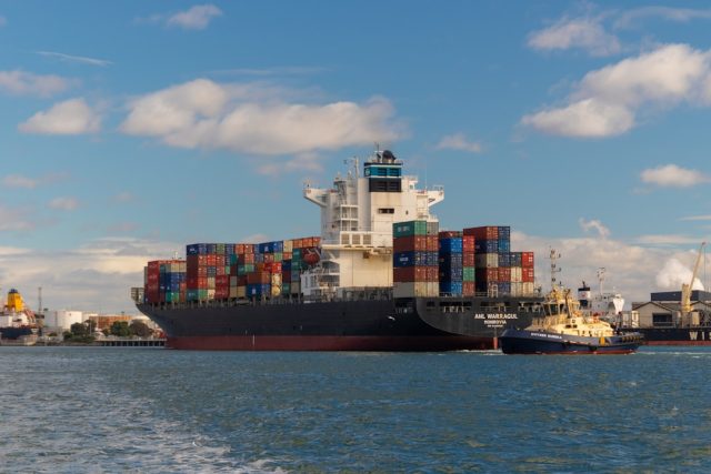 Congress Gave Away Tariff Power Through 1962 National Security Law A busy US port with cargo ships and stacked metal containers, illustrating the impact of new tariffs on imported goods.