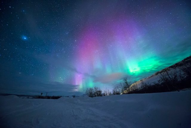 Sunspot Cycle Peak Triggers Rare G5 Geomagnetic Storm Across Globe Aurora borealis lights up the night sky during a G5 geomagnetic storm, with green and purple hues over a landscape.