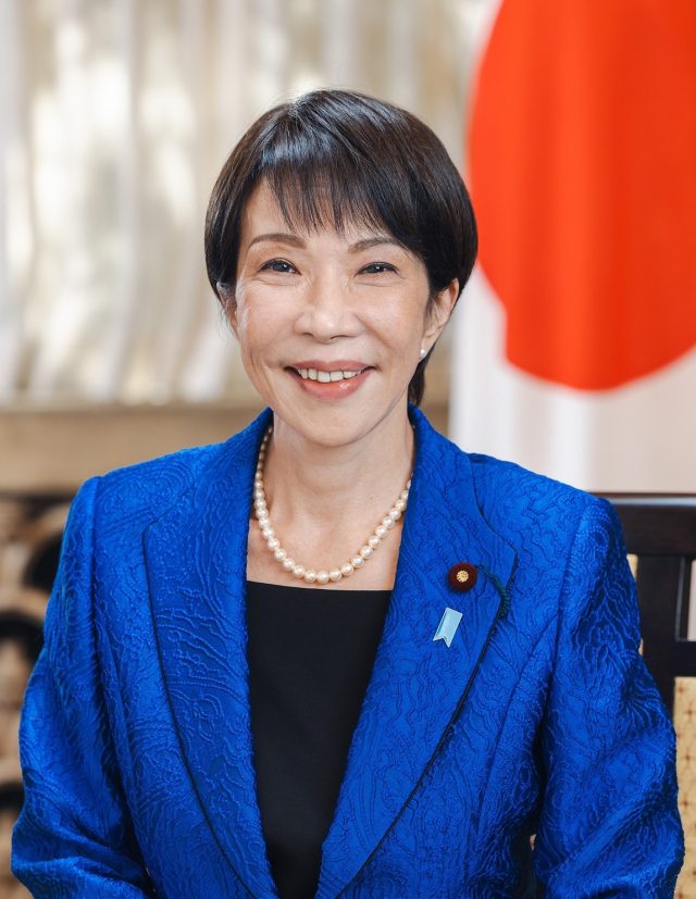 Sanae Takaichi Reappointed as Japanese Prime Minister by House of Representatives Sanae Takaichi stands at the parliamentary podium smiling while lawmakers applaud her re-appointment as Japan's first female Prime Minister.