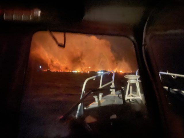 Directed-energy weapon wildfire conspiracy theories Smartphone screen shows viral laser wildfire claim while actual flames rage behind power lines in Los Angeles.