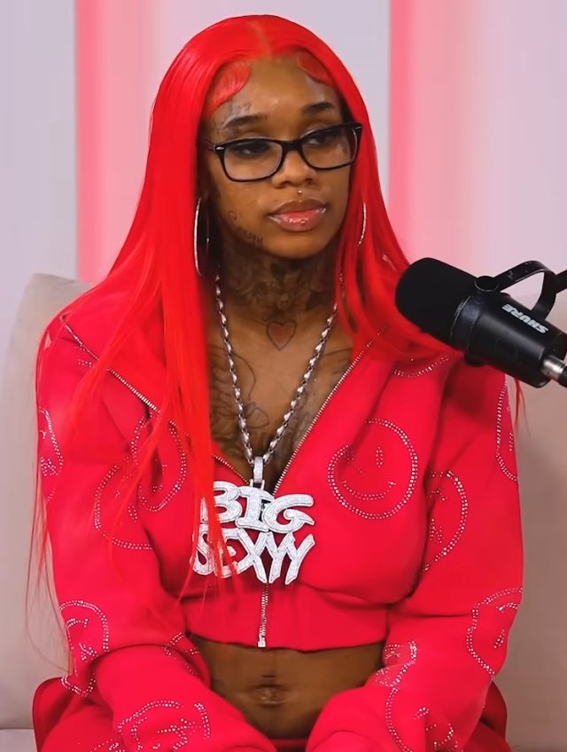 Hood Hottest Princess Sexyy Red poses in studio, neon lights framing her new Hood Hottest Princess mixtape cover art on wall behind.