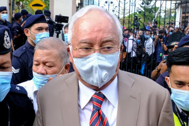 Najib Razak Corruption Trial Malaysia Former Malaysian Prime Minister Najib Razak speaking at a political event, surrounded by supporters and Malaysian flags.