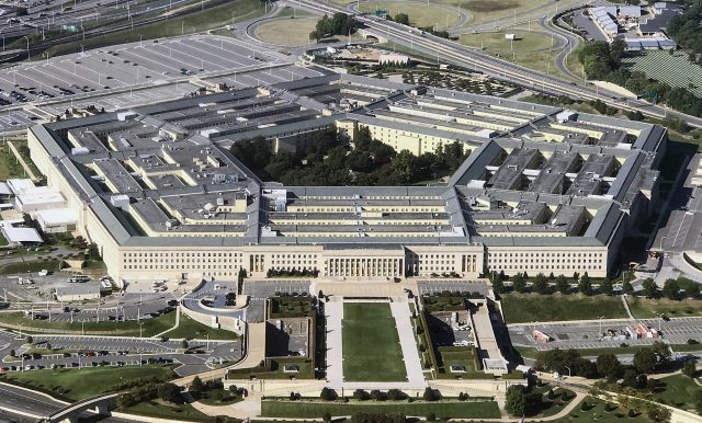 Pentagon Building Redacted Pentagon email printout with subject line visible beside magnifying glass on dark desk.