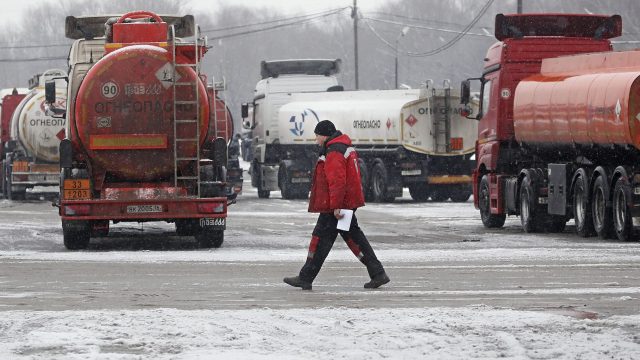 Russian Diesel Tanker Europe Ban Rows of diesel pumps at an EU truck stop display prices while a cargo tanker flies the Russian flag in the background.